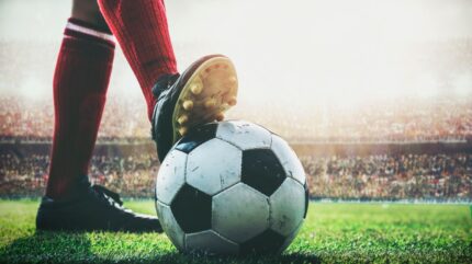 بازیکن فوتبال در زمین چمن توپ را زیر پای خود نگه داشته است.