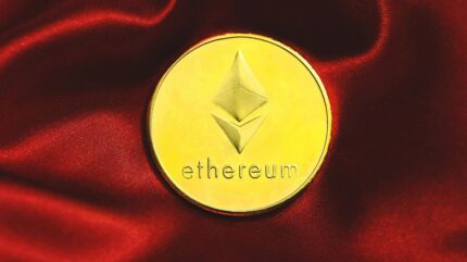 سکه‌ی طلایی ارز دیجیتال اتریوم روی یک پارچه‌ی قرمز.