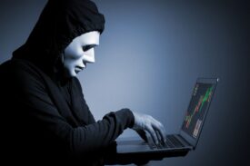 یک هکر با نقاب سید در حال کار با لپ‌تاپ است.
