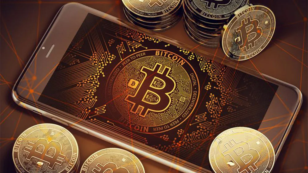 یک گوشی موبایل با لوگوی بیتکوین در کنار سکه‌های بیت کوین